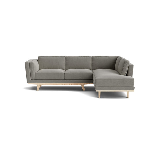 The Kirnik Bumper Sectional in Natural Latex is a contemporary L-shaped sofa with a muted gray color, featuring a left-side chaise. It boasts a minimalist design with cushioned seats and wooden legs, set against a plain white background.