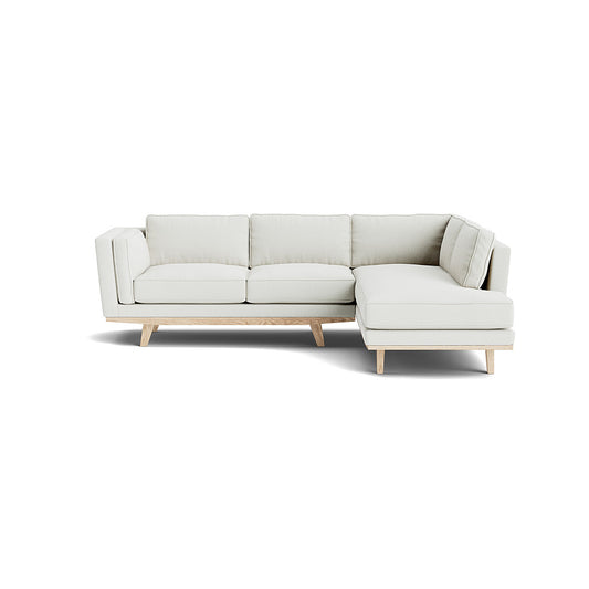 The Kirnik Bumper Sectional in Natural Latex is a modern L-shaped sofa featuring light grey upholstery and wooden legs, set against a plain white background.