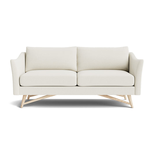 Introducing the Gio Sofa in Natural Latex: a cream-colored, modern design featuring two seat cushions and two back cushions. It showcases distinctive sloped armrests, along with an exposed geometric wooden frame at the base, all set against a plain white background.