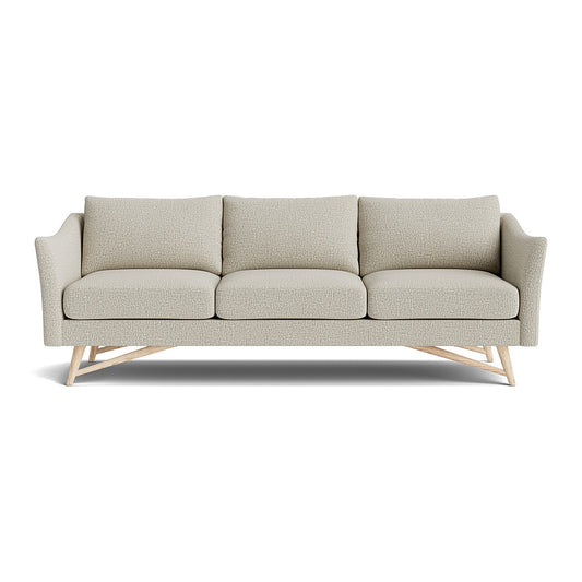 The Gio Sofa in Natural Latex is a modern piece with three seat cushions and a wooden base, designed in light gray. It features minimalist aesthetics with slightly angled armrests.