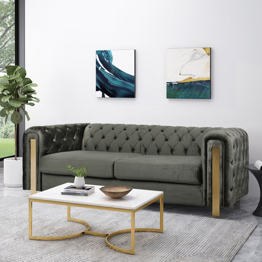 Elegant living room featuring a gray Comfy 3 Sofa with tufted back and arms, complemented by gold accents. A white marble coffee table is adorned with a small plant. Two abstract paintings hang above the sofa while a large window and an indoor plant brighten the space.