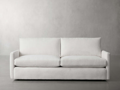 The Kipton 84" Deep Sofa, featuring a sleek and modern design with clean lines, is showcased against a plain, light gray background. Its minimalist white color and plush cushions contribute to its contemporary style.