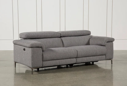 The Talin Power Reclining Sofa with USB, featuring adjustable headrests and sleek metal legs in modern grey fabric, is positioned against a white paneled wall, offering a contemporary design on a polished concrete floor.