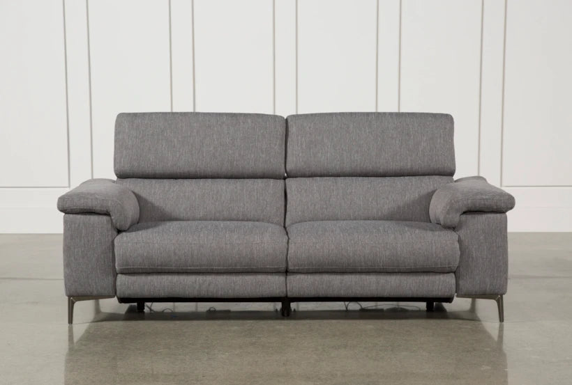 A gray, modern Talin Power Reclining Sofa with USB and soft cushioning is set on a polished concrete floor. It features a sleek, minimalist design in its backrest and armrests. The wall behind boasts white vertical panel detailing.