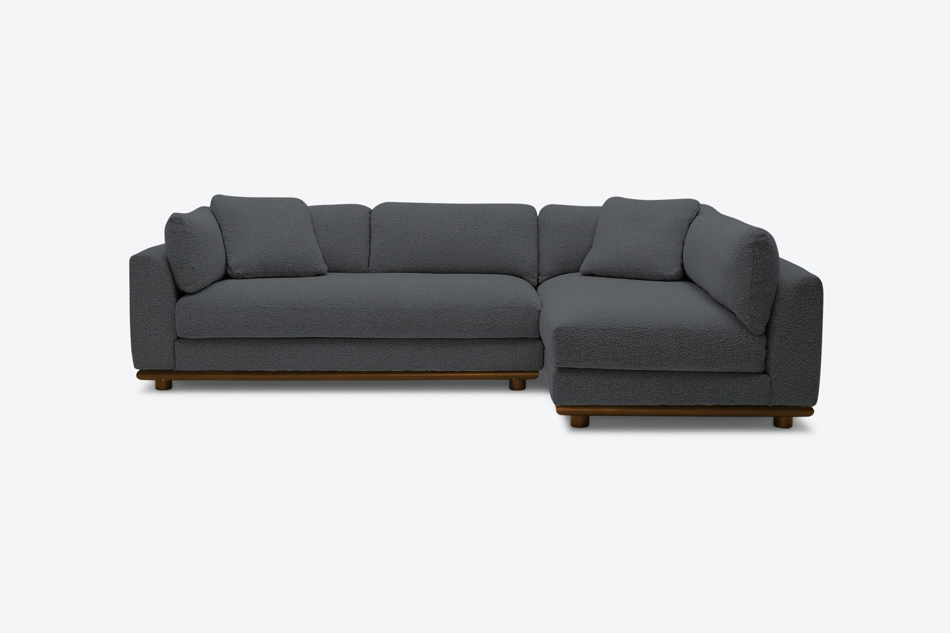 The Miller Sectional is a contemporary dark gray L-shaped sofa with a wooden base and short legs, showcasing plush cushions and a minimalist design, positioned against a plain light background.