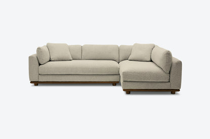 A contemporary Miller Sectional in light gray, featuring an L-shaped design with plush cushions and wooden legs, displayed against a simple, light backdrop.