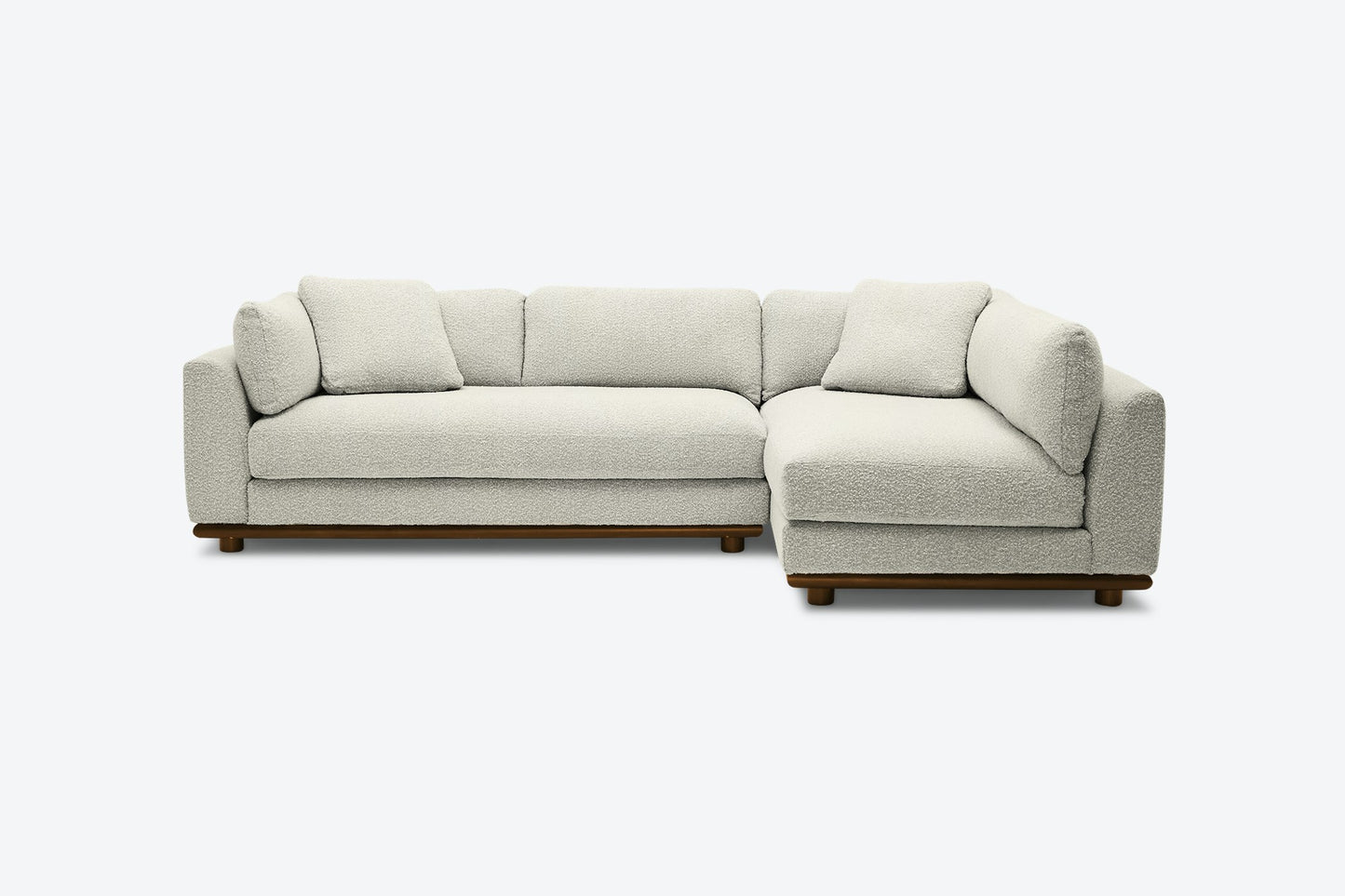 The Miller Sectional is a contemporary L-shaped sofa in light gray, showcasing a minimalist design with plush cushions and a low-profile wooden base, set against a plain white background.