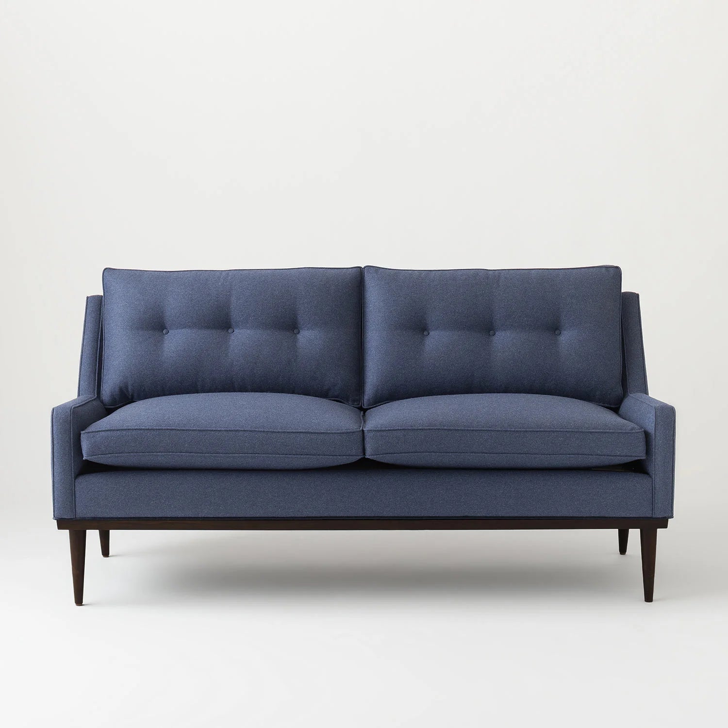 Introducing the Jack Sofa: a modern, mid-century style sofa featuring blue upholstered fabric and dark wood legs. This stylish piece boasts a tufted backrest and two large seat cushions, beautifully set against a plain light gray background.