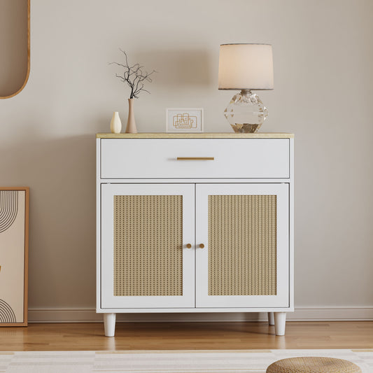 A white cabinet with a drawer and two rattan doors (Cat Litter Box Enclosure) stands against a beige wall, topped with a geometric lamp, vase of twigs, and abstract artwork. The room has wooden floors and a woven rug.