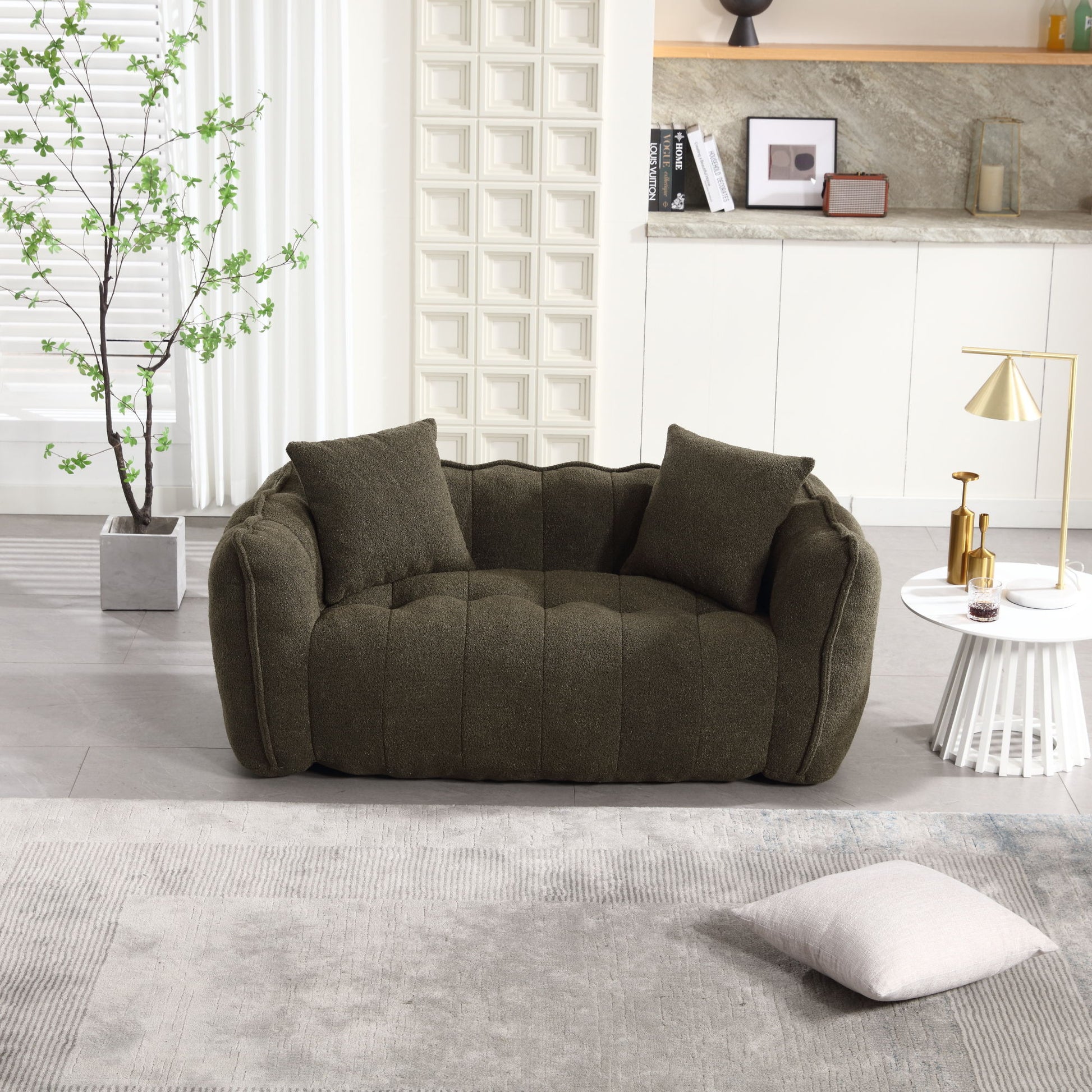 A cozy, deep green sofa with tufted cushions rests in a bright living room featuring the Soft Beanbag Chair with High Resilience Foam Core for Two People. A white round side table holds a lamp and decor. Nearby, a pillow lies on a gray rug, and plants add greenery to the modern, inviting space.