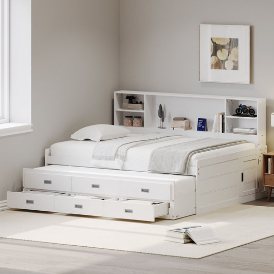 A Captain Daybed with trundle and three storage drawers is set against a wall featuring a storage bookcase headboard. Above hangs a decorative frame, while natural light streams through the window, accentuating the neutral decor and soft rug on the floor.