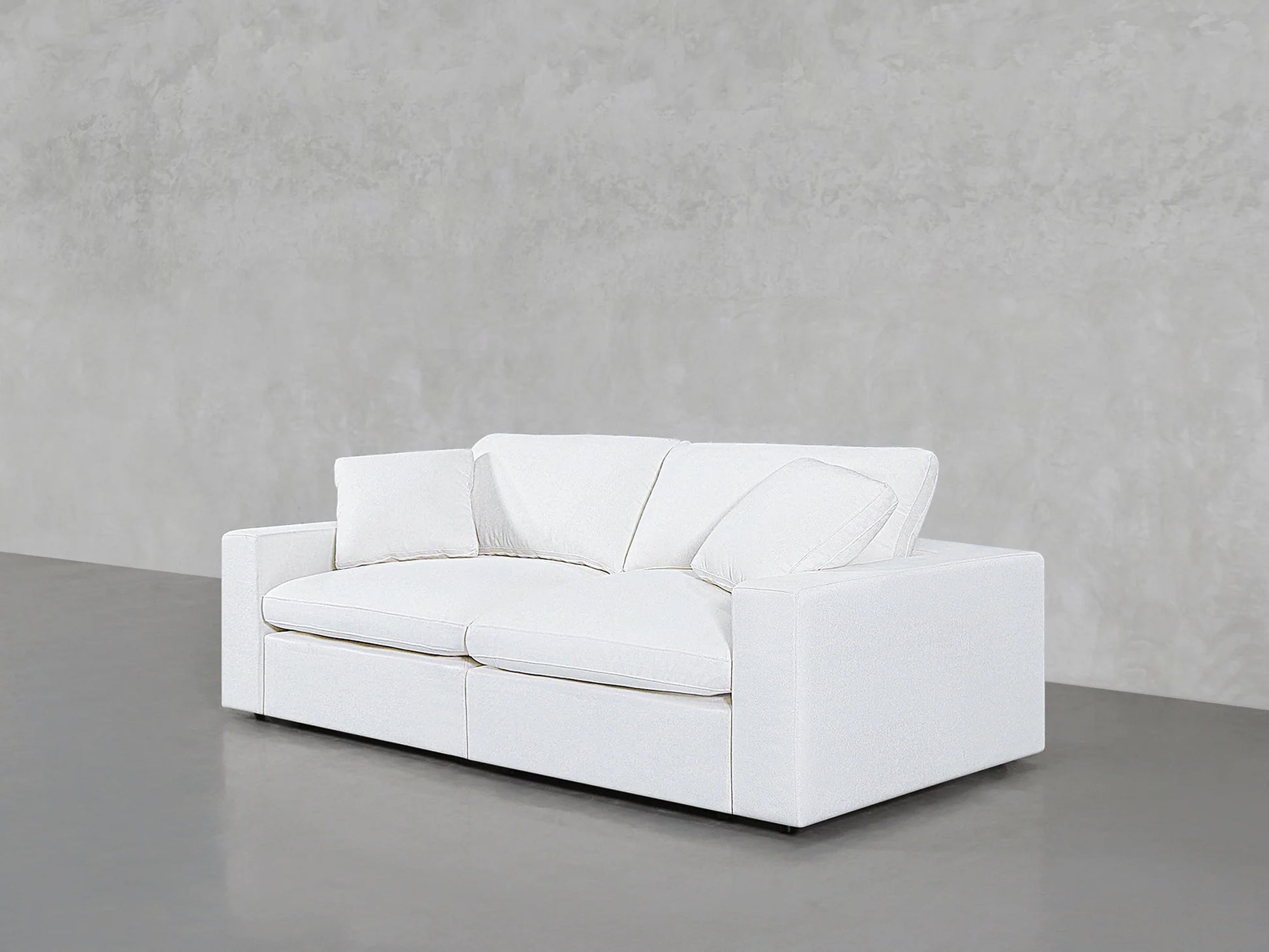 A sleek 2-Seat Modular Loveseat in white, featuring dual seat and back cushions, is positioned against a plain gray wall. The floor is smooth and slightly reflective, complementing the room's minimalist aesthetic.