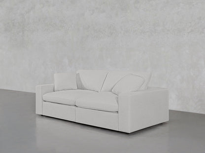 A 2-Seat Modular Loveseat in a minimalist light gray fabric, featuring two seat cushions and two back pillows, is positioned against a matching light gray wall on a polished concrete floor.