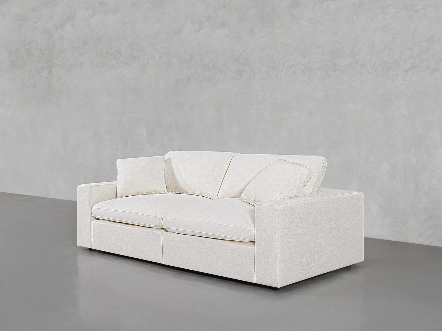 A 2-Seat Modular Loveseat, featuring a modern white design with clean lines and plush cushions, sits on a smooth gray floor against a textured light gray wall.