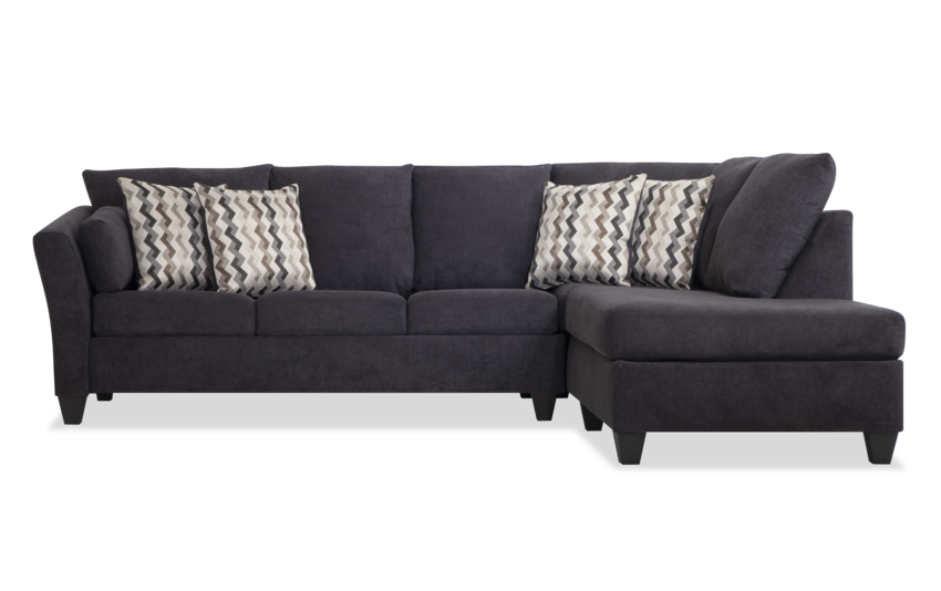 The Virgo Charcoal 119'' 2 Piece Chaise Sectional, with its dark gray hue and right-side chaise section, sits against a white background. It features a clean, modern design and includes five patterned throw pillows showcasing a chevron pattern.