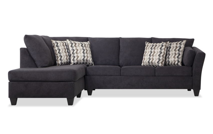 Introducing the Virgo Charcoal 119'' 2 Piece Chaise Sectional, a stylish dark gray sectional sofa featuring three spacious seats and a left-facing chaise lounge. It comes with four decorative pillows, showcasing an elegant chevron pattern in shades of gray and white.