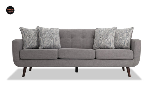 The Bettie 86'' Sofa is a modern piece in gray, featuring three seat cushions and five patterned throw pillows. It has wooden legs and a rectangular, tufted design on the backrest. A small round "GQ Loves This" tag is visible in the upper left corner.