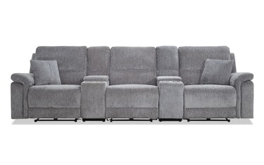 A spacious Renegade Gray 125'' power reclining sectional with a textured fabric finish, featuring multiple reclining seats, armrests, and two built-in cup holders. Two matching throw pillows add comfort to the seating area. The sectional is elegantly positioned on a smooth, white floor.