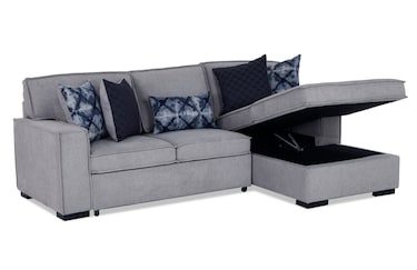 The Playscape Gray 94'' 2 Piece Pop-Up Sleeper Chaise Sectional features a storage chaise that lifts open, and is complemented by patterned and plain dark gray pillows, providing a modern and functional seating solution.