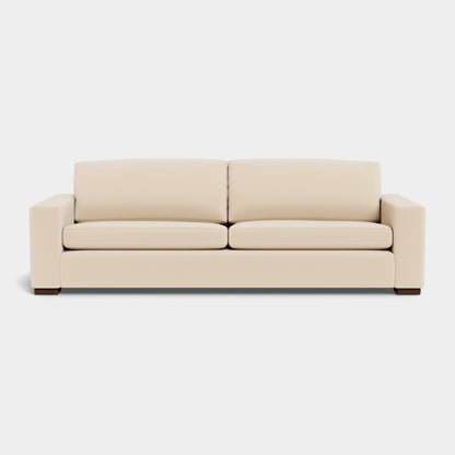 The Barton Sofa is a beige, modern piece with two seat cushions and two back cushions. It boasts a sleek and minimalist design, accentuated by wide armrests and wooden legs, all set against a plain, light background.