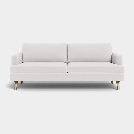 The Lido Sofa, featuring a minimalist and elegant design with a modern white finish, comes complete with two cushions and four gold-colored legs. It is perfect for contemporary interiors and looks stunning against a plain light background.