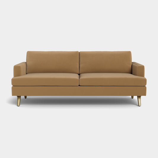 The Lido Sofa is a modern piece featuring tan upholstery with clean lines, square cushions, and slim gold legs, all set against a white background.