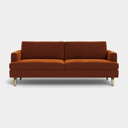 Experience the elegance of the Lido Sofa, a contemporary brown velvet piece with plush cushions and a sleek design. This sofa boasts two wide seats and is supported by four short, angled gold legs. Set against a plain white background, its simplicity and refined style are beautifully highlighted.