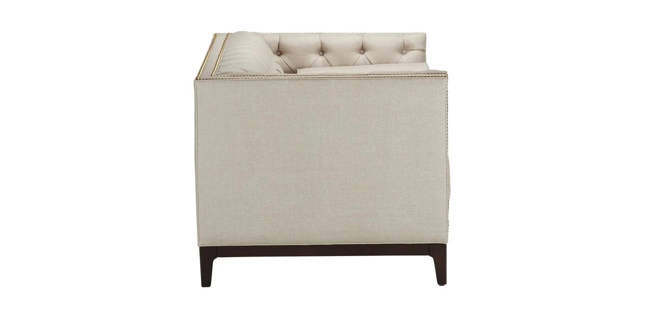 Side view of an Anderson Loveseat in beige, featuring tufted upholstery with nailhead trim and dark wooden legs, set against a white background.