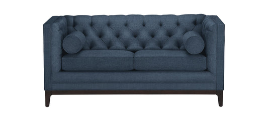 The Anderson Loveseat is a blue, tufted sofa with two cushions on each side. It features dark wooden legs and a boxy design, offering a modern and elegant look.