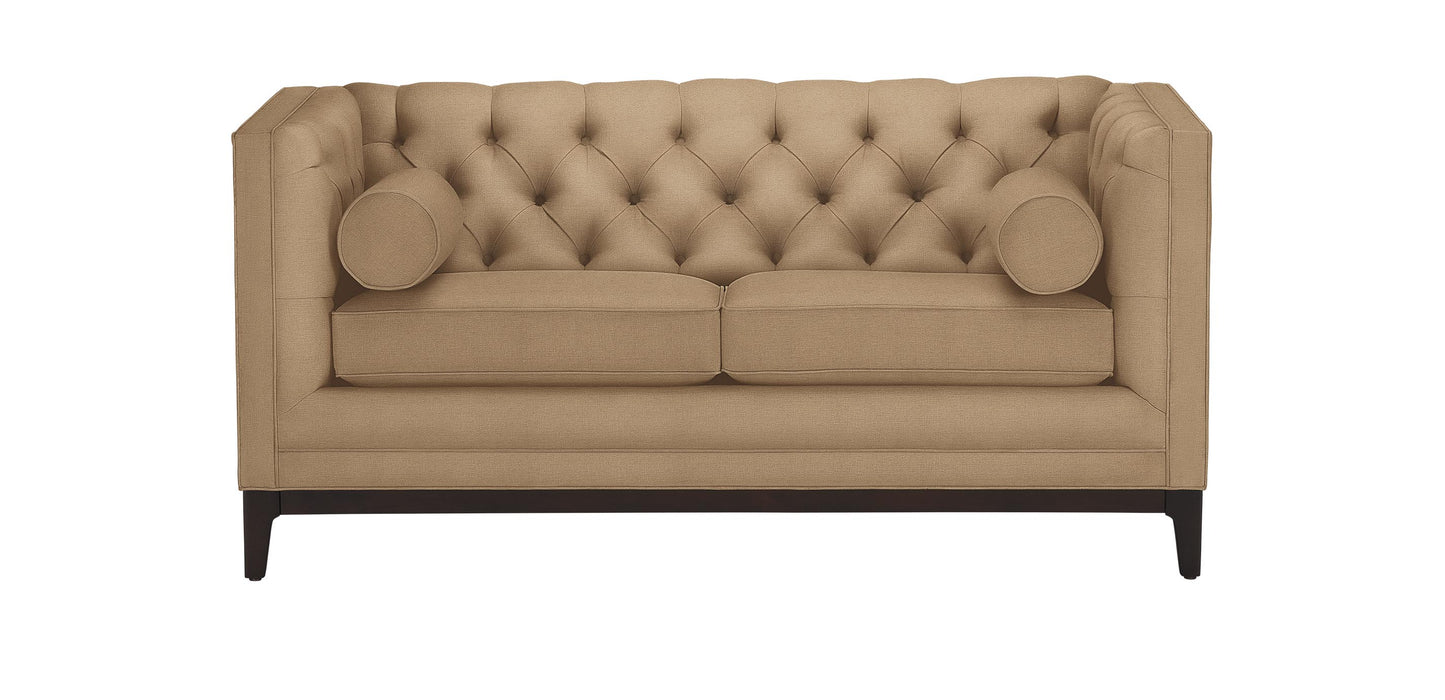 The Anderson Loveseat is a beige tufted design featuring a high back and sides. It comes with two seat cushions, two cylindrical accent pillows, and is supported by dark wooden legs.