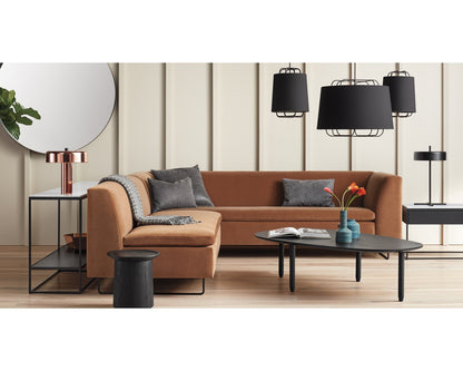 A modern living room featuring the Bonnie and Clyde Sectional Sofa with gray cushions, complemented by black and copper lamps, a stylish round wall mirror, a sleek black coffee table adorned with red flowers, and a side table holding a potted plant to enhance the contemporary decor.