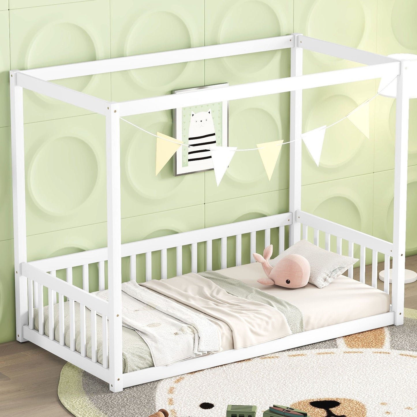 In a child's bedroom, the Canopy Frame Floor Bed With Fence, Guardrails stands against a pastel green wall. It features a small white rail, adorned with a pink stuffed whale and triangular flags above. The light wood floor is accented by a round, colorful rug.