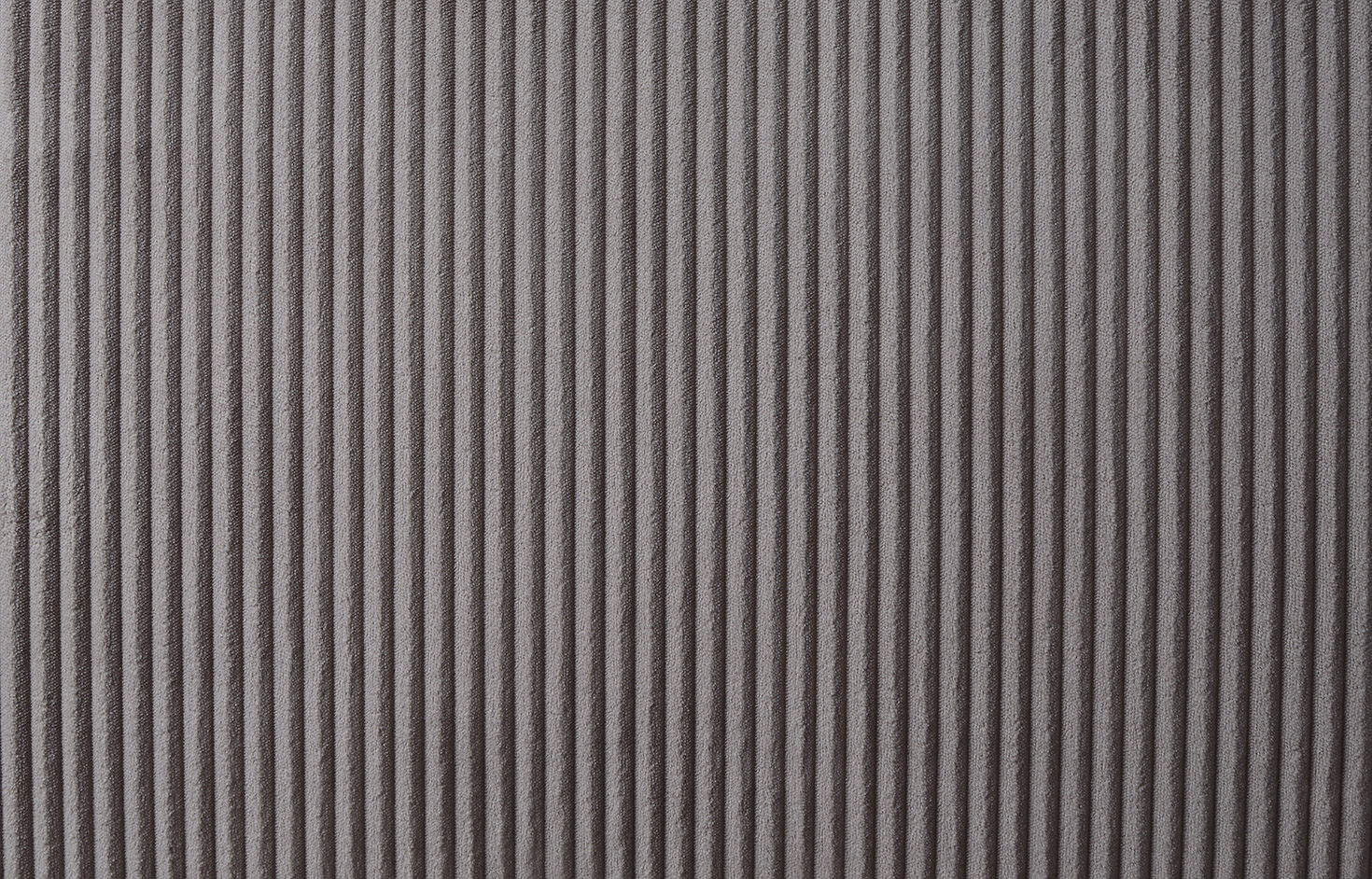 Close-up of a textured surface with vertical ridges in a soft, brown fabric, resembling the Justine Corduroy Convertible Sleeper Loveseat. The ridges cast a pattern of shadows and highlights, enhancing depth and visual interest in the monochromatic design.