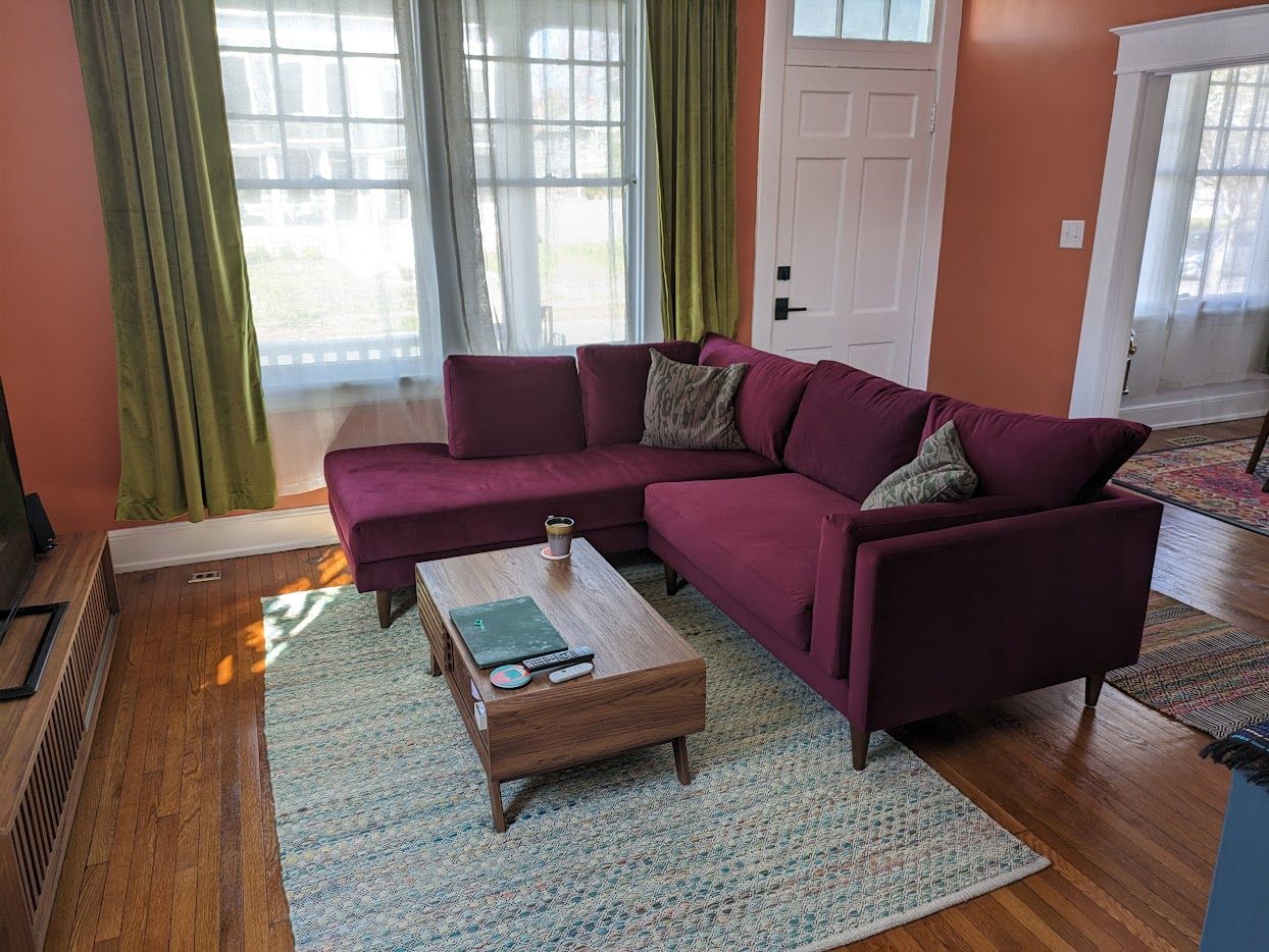 A dark red/ maroon sectional sofa sits on top of a blue-green textured rug with a wooden coffee table. 