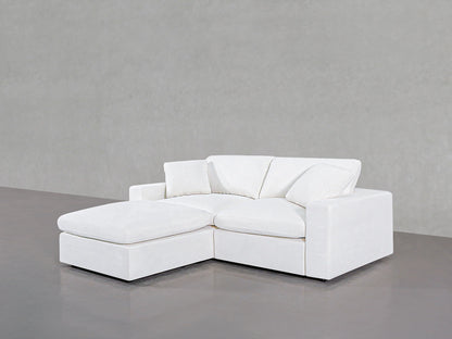 A 3-Seat Modular Chaise Sectional in a minimalist white design, featuring a chaise lounge on the left side, is set against a plain gray background. This sofa boasts clean lines and includes three matching throw pillows.