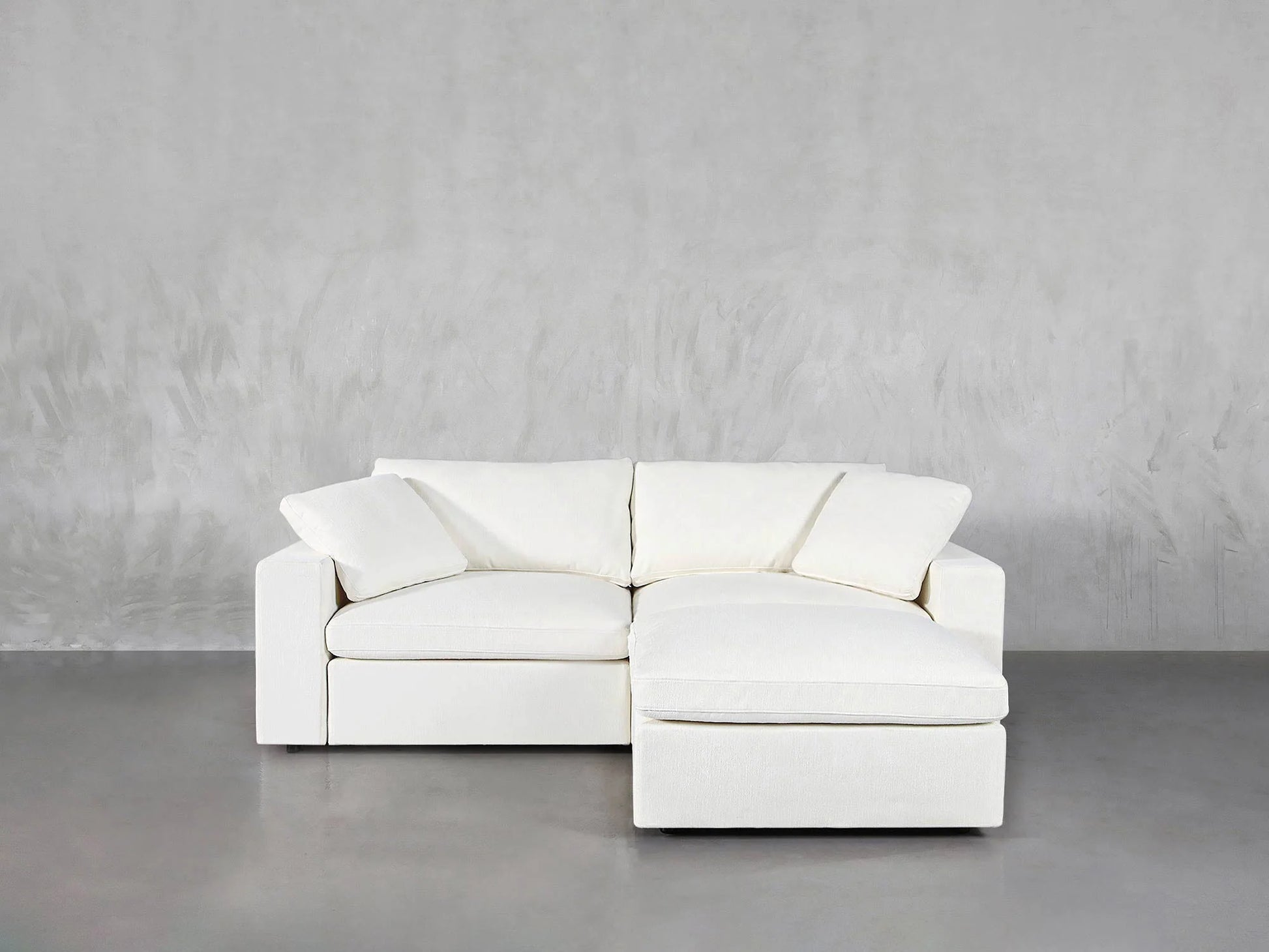 A 3-Seat Modular Chaise Sectional in a modern, white design is positioned against a light gray textured wall on a smooth gray floor.