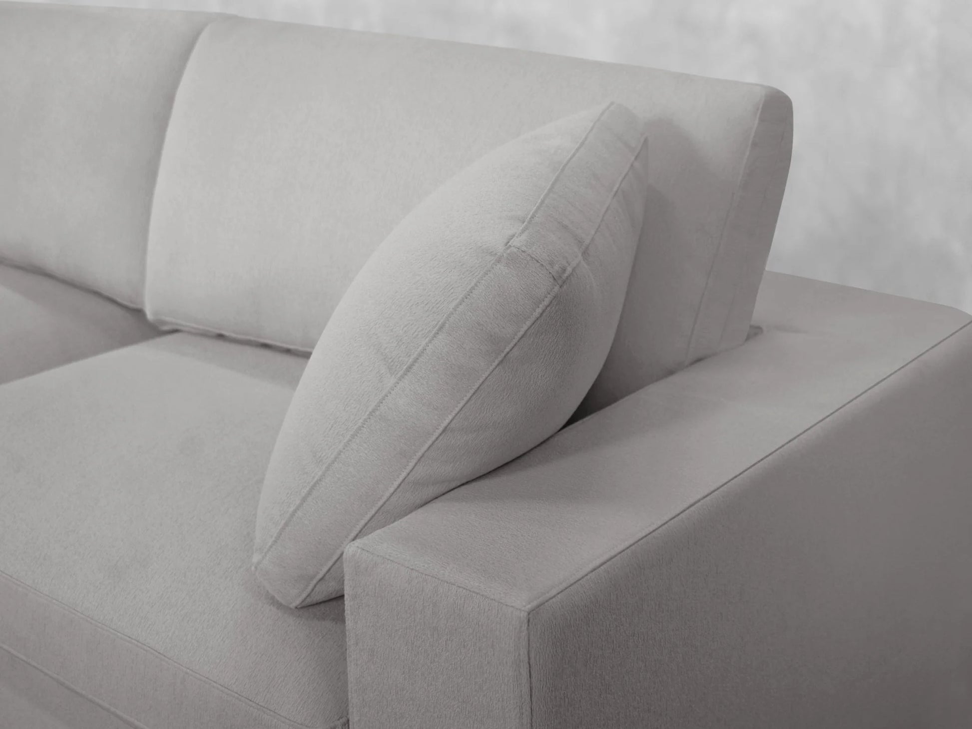 A close-up view of the 3-Seat Modular Chaise Sectional in light gray, featuring a matching cushion leaning against the backrest. The upholstery looks soft and plush, and the sectional is set against a light, neutral background.