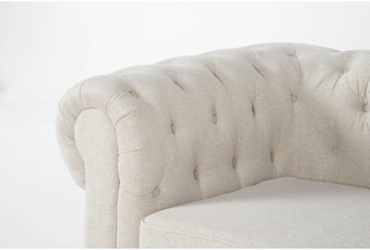 Close-up of the Elis Wheat 73 Inch Chesterfield Loveseat featuring beige tufted upholstery with a rolled armrest. The fabric exhibits a textured look, while the tufting enhances its classic appeal. The background is stark white.