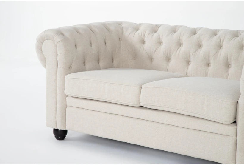 The Elis Wheat 73 Inch Chesterfield Loveseat, featuring a tufted back, rolled arms, and two seat cushions in beige, is set against a plain light background. This loveseat showcases dark wooden legs and boasts a classic, elegant design.