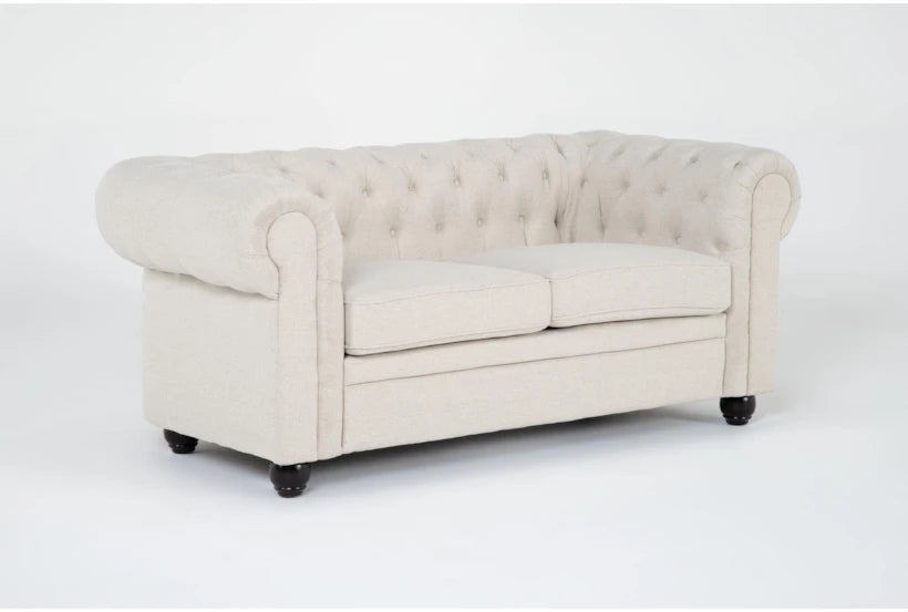 The Elis Wheat 73 Inch Chesterfield Loveseat, with its light beige upholstery, tufted backrest, and rolled arms, includes two seat cushions. It is showcased standing on dark wooden legs against a plain white background.