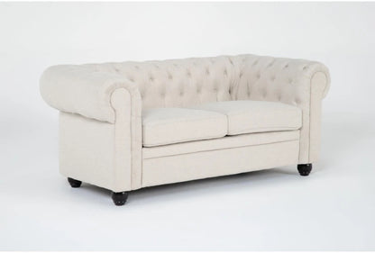 The Elis Wheat 73 Inch Chesterfield Loveseat, with its light beige upholstery, tufted backrest, and rolled arms, includes two seat cushions. It is showcased standing on dark wooden legs against a plain white background.