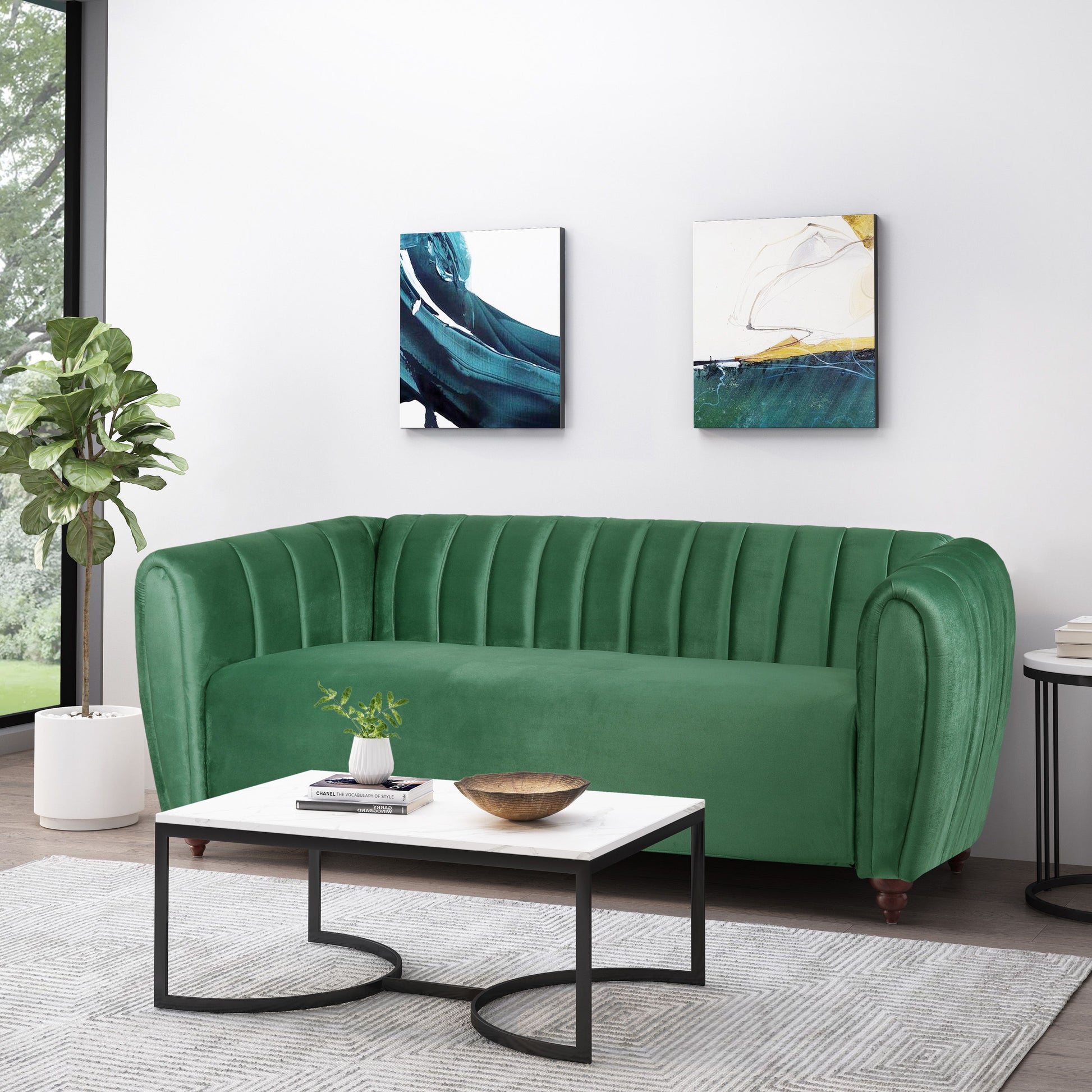 A modern living room features a 3 Seater Sofa Modern Glam Design in green velvet, a white and black coffee table with a plant and bowl, two abstract paintings on the walls, and a potted plant by the window enhancing the natural light.