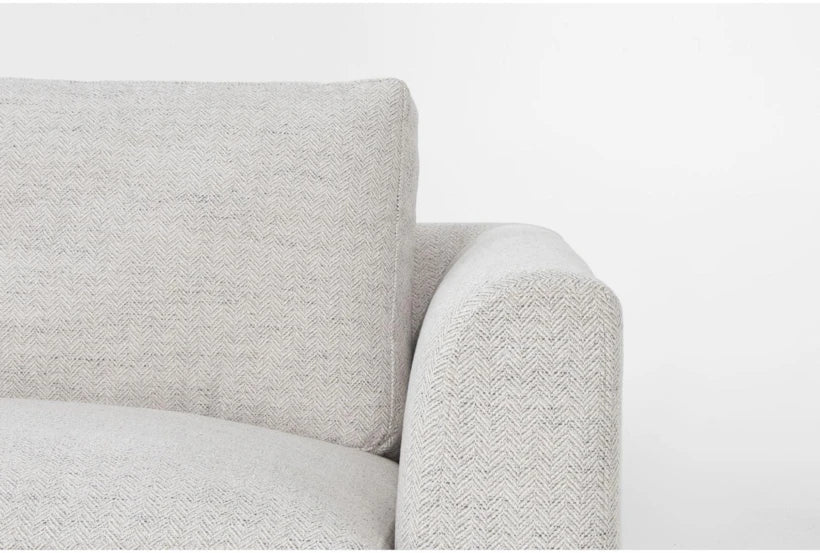 Close-up of a beige chenille sofa. The fabric features a subtle herringbone pattern. The image showcases the sofa's cushion and armrest against a plain white background.