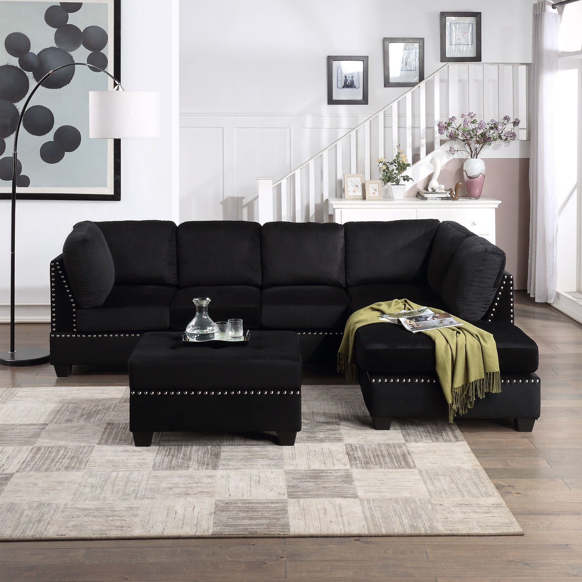 A modern living room featuring a Reversible Sectional Sofa with rivet trim, space-saving storage ottoman, and green throw. A geometric rug covers the wooden floor, while wall art, framed photos, and a large floor lamp enhance the ambiance.