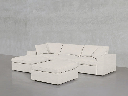 A 4-Seat Modular Chaise Sectional with Ottoman in a neutral hue is placed against a textured gray wall. The furniture features clean lines and a modern design, sitting on a plain gray floor.