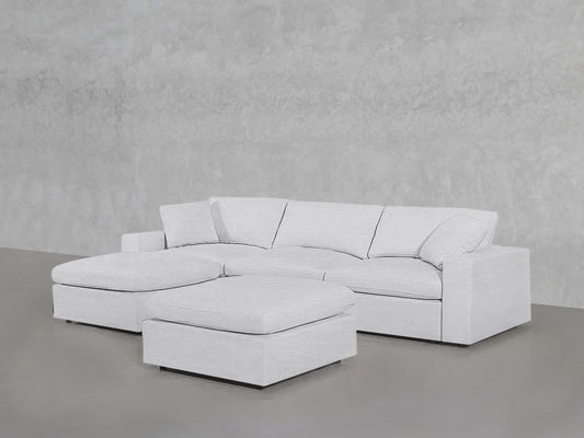 In a minimalist setting featuring a textured gray wall and floor, the 4-Seat Modular Chaise Sectional with Ottoman stands out with its light-gray tones. The sofa showcases clean lines and plush cushions, contributing to a modern and inviting atmosphere.