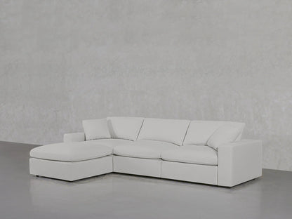 A 4-Seat Modular Chaise Sectional is positioned against a plain, light gray wall with a polished concrete floor. Its multiple seat and back cushions give it a modern and minimalist appearance.