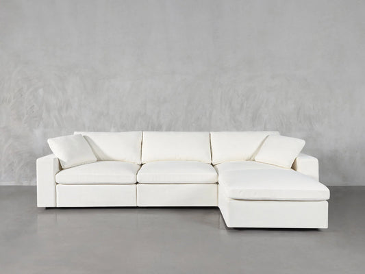 The 4-Seat Modular Chaise Sectional, in a spacious white design, features three cushions and a right-side chaise lounge. It's set against a light gray background and exudes a plush, modern look with two matching pillows placed at each end.