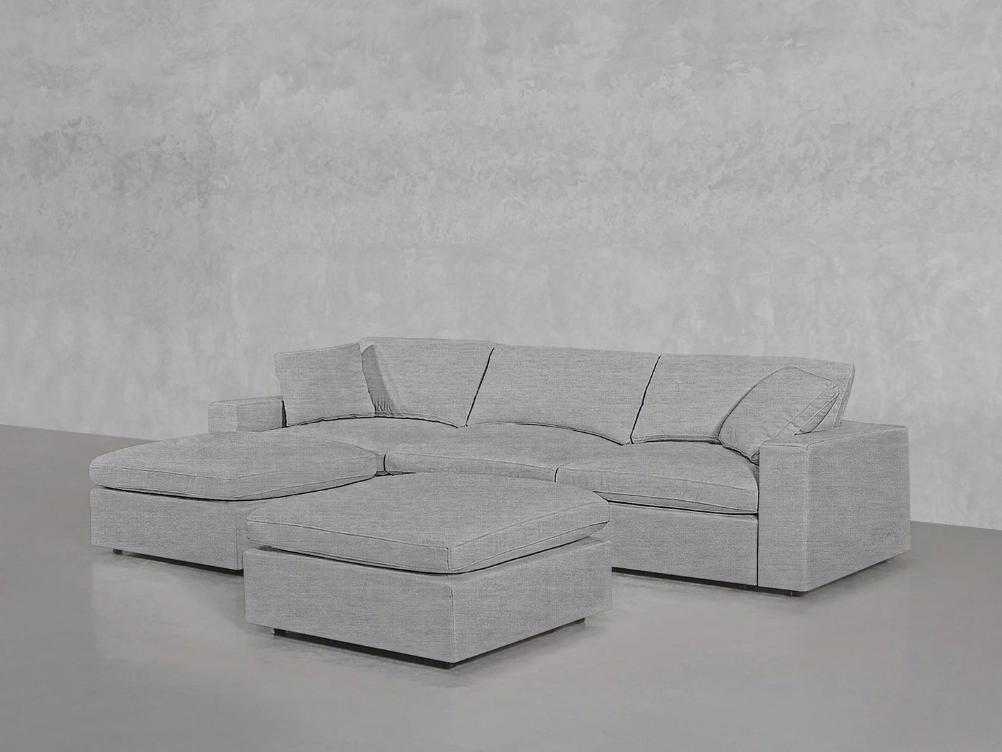 A stylish 4-Seat Modular Chaise Sectional with Ottoman in a modern gray color is set against a textured gray wall and smooth gray floor. The sectional features a left-side chaise and boasts a minimalist design.