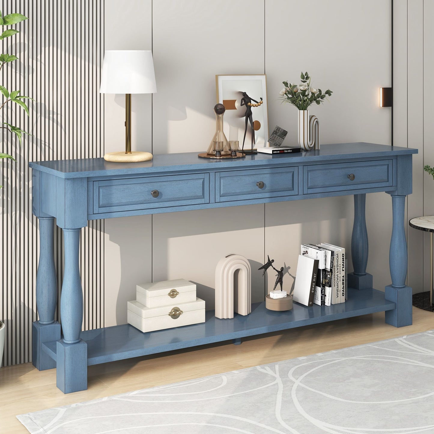 The "Long Console Table With Drawers And Shelf For Entryway, Hallway, Living Room" features blue wood with three drawers and a lower shelf. Items on top include a white lamp, small sculptures, and a plant. The shelf holds boxes, books, and decor against a light gray wall with a circular-patterned rug.